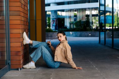 Genç çıplak ayaklı kız asfaltta oturuyor.