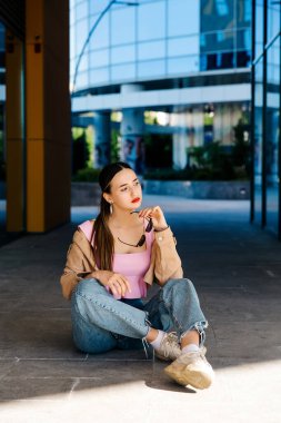 Genç çıplak ayaklı kız asfaltta oturuyor.