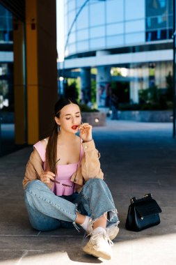 Genç çıplak ayaklı kız asfaltta oturuyor.