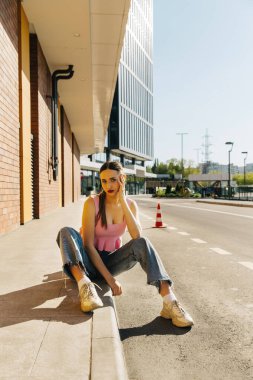 Genç çıplak ayaklı kız asfaltta oturuyor.