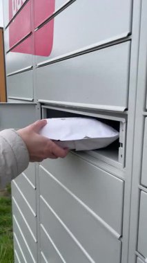 Paketi paket dolabına yerleştirip dolap kapısını kapatan bir elin yakın çekimi. Doğal ışıklandırma, teslimat, teslimat ve son mil lojistiği taşır.