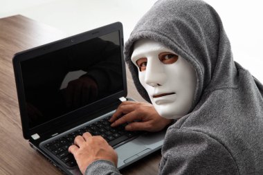 Maskeli hırsız laptop 'dan kişisel bilgileri çalıyor. Hackleme kavramı.