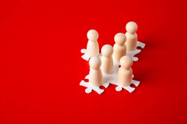 Takım oluşturmanın sembolü olarak kırmızı arkaplandaki yapbozların tahta figürleri. Organizasyon grubu insanları iş başında. İşbirliği ve ortaklık.