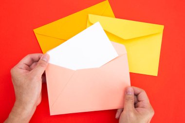 Elinde renkli zarfta beyaz bir kart var.