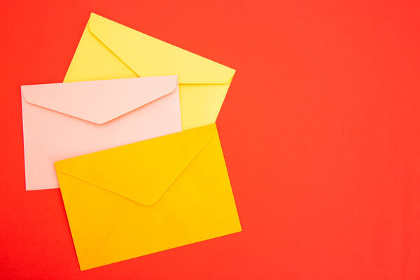Colorful paper envelopes on red background - top view