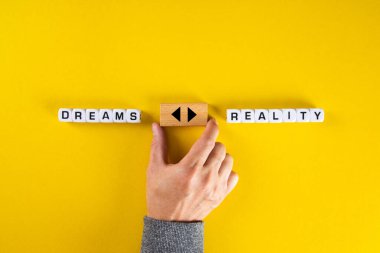 Rüyalar ve gerçeklik seçenekleri arasında ok ikonlu tahta bir küp tutan eller. Hayallerin peşinden gitmek ya da gerçeklik ikilemiyle yüzleşmek..