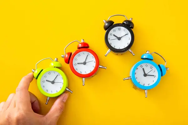 独立した黄色の背景に緑の目覚まし時計を選ぶ手 — ストック写真