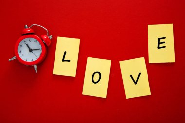 Kırmızı alarm saati ve sarı yapışkan notlar kırmızı arka planda aşkı gösteriyor.