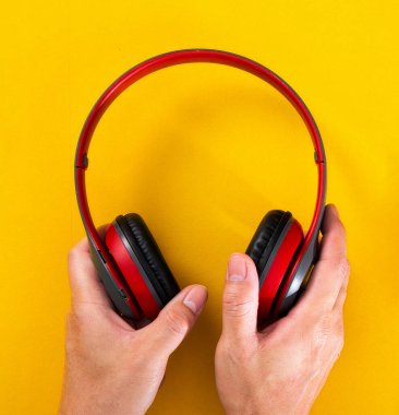 Eller canlı sarı bir yüzey üzerinde modern kırmızı kablosuz kulaklıkları tutuyor.