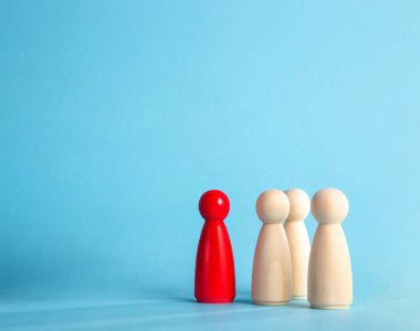 Kırmızı ahşap figür, mavi arka planda üç doğal tahta figürü yönetiyor.