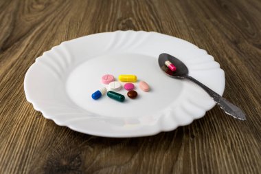 Tahta masada tabletlerle dolu beyaz bir tabak var..