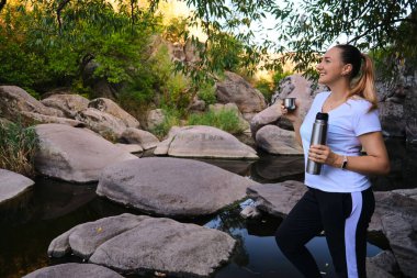 Seyahat, eğlence ve yaşam tarzı konsepti. Aktif kadın turist takım elbise giyer, havasında olur, manzaralı yerleri keşfeder, termostan sıcak çay içer.