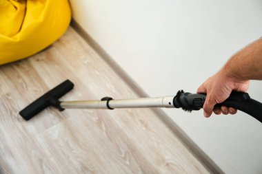 Adam odanın zeminini elektrikli süpürgeyle temizliyor, birinci kişinin üst görüntüsü.
