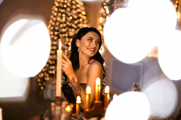 party, drinks, holidays, people and holiday concept - smiling woman in evening dress with a glass of sparkling wine over Christmas tree lights background