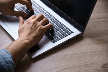 Adamın elleri dizüstü bilgisayarda klavyede daktilo kullanıyor. Çalışan genç bir adamın kırpılmış görüntüsü