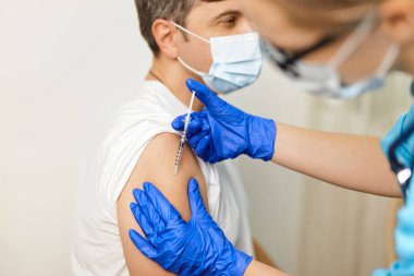 Genç kadın doktor Coronavirus Covid 'e karşı aşı yaptırıyor. 19 yaşında, klinikteki genç bir adama.