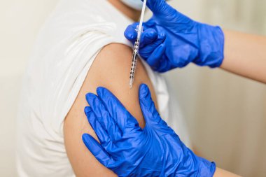 Doktorun elini kapat Coronavirus Covid 'e karşı aşı yap. 19 yaşında, klinikteki genç bir adama.