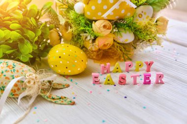 Beyaz ahşap arka planda yumurtaları olan renkli bir Paskalya sepeti, çiçek pınarıyla süslenmiş. Bahar tatili tebrik konsepti..