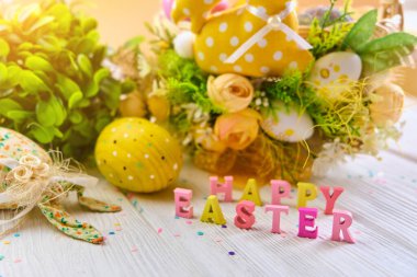 Beyaz ahşap arka planda yumurtaları olan renkli bir Paskalya sepeti, çiçek pınarıyla süslenmiş. Bahar tatili tebrik konsepti..