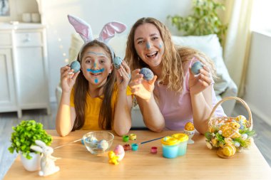 Anne ve kızı boyalı yumurtalarla oynuyorlar. Mutlu aile Paskalya için hazırlanıyor. Tavşan kulağı takan şirin bir kız çocuğu..