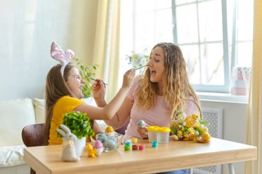 Anne ve kızı yumurta boyuyor. Mutlu aile Paskalya için hazırlanıyor. Tavşan kulağı takan şirin bir kız çocuğu..