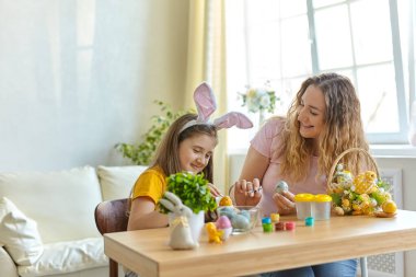 Anne ve kızı yumurta boyuyor. Mutlu aile Paskalya için hazırlanıyor. Tavşan kulağı takan şirin bir kız çocuğu..