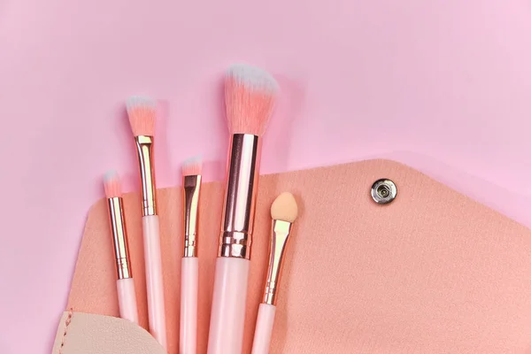 Make up brushes spilling out of a beige cosmetics bag on pastel pink background. Top view. Flat lay. Beauty concept. pink color background, close up view, copy space.