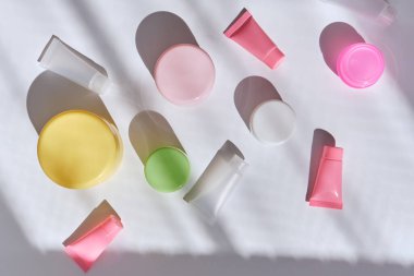 Renkli kavanoz setinde yüz kremi ve beyaz masa arka planında tüpler. Sert ışık, gölge. Cilt ve vücut bakımı için doğal güzellik ürünleri. Yaz yaşam tarzı. Üst görünüm, alanı kopyala