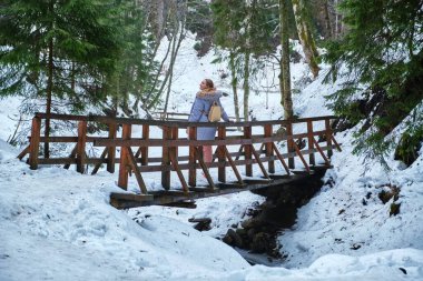 Kışın, karlı dağ geçidinde uzun tahta bir köprüde yürüyen beyaz bir kadının arkasında. Genç kız bilinmeyen yerlere doğru tek başına yürüyor..