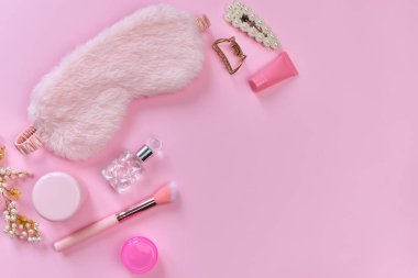 Uyku maskesi, bakım ürünleri, kadın aksesuarları, parfüm, saç tokaları ve pembe arka plandaki kadın eşyaları. Günlük cilt bakım konsepti. Üst görünüm, düz görünüm, kopyalama alanı