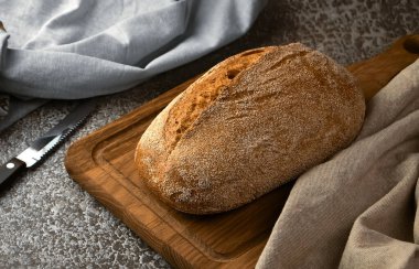 Kesme tahtasında tam tahıllı çavdar ekmeği ve gri arka planda bıçak. Seçici odak