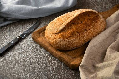 Kesme tahtasında tam tahıllı çavdar ekmeği ve gri arka planda bıçak. Seçici odak