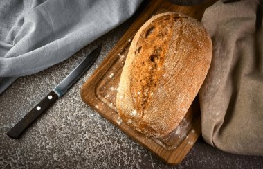 Kesme tahtasında tam tahıllı çavdar ekmeği ve gri arka planda bıçak. Seçici odak