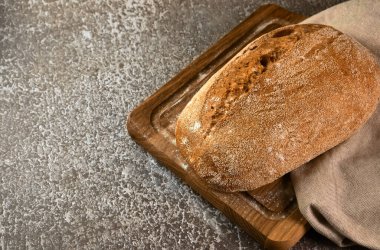 Gri arka planda kesme tahtasına tam tahıllı çavdar ekmeği. Seçici odak, metin için alanı kopyala