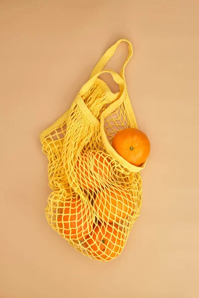 oranges in a string bag on beige background. Healthy lifestyle. Top view. Zero waste.