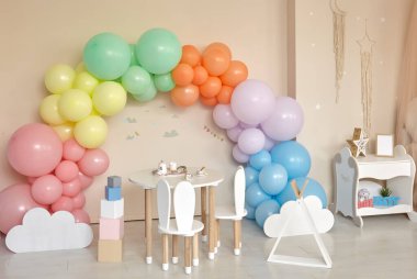 Küçük masa ve çocuk odasının içinde tavşan kulaklı sandalyeler. Gökkuşağı, renkli balon kemeri, bayram, doğum günü, parti onuruna dekorasyon