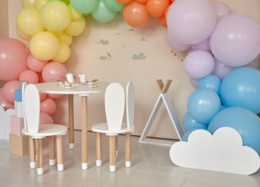 Küçük masa ve çocuk odasının içinde tavşan kulaklı sandalyeler. Gökkuşağı, renkli balon kemeri, bayram, doğum günü, parti onuruna dekorasyon