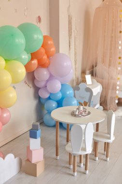 Küçük masa ve çocuk odasının içinde tavşan kulaklı sandalyeler. Gökkuşağı, renkli balon kemeri, bayram, doğum günü, parti onuruna dekorasyon