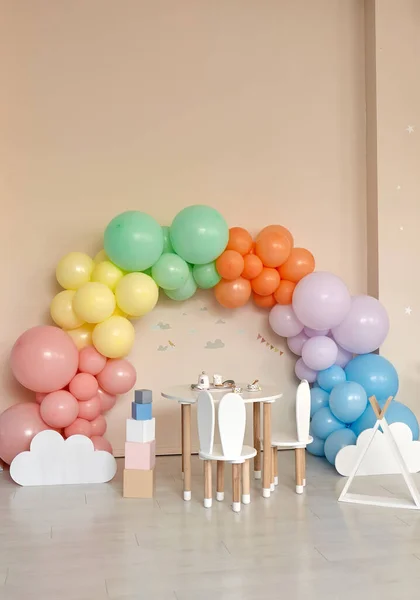 Small table and chairs with bunny ears in children\'s room interior. Rainbow, colorful balloon arch, decoration in honor of the holiday, birthday, party