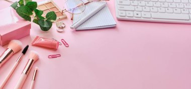 Banner Flat, modern ofis masasının üst görüntüsü. Çalışma alanı klavye, not defteri, gözlük, kalem pembe arka planda güzellik aksesuarları. Çevrimiçi iş, alışveriş, kurslar ve eğitim kavramı