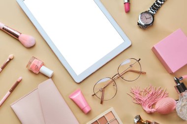 Düz yatıyordu, modern ofis masasının üstündeydi. Çalışma alanı beyaz tablet, not defteri, gözlükler, kalemler, pastel bej arka planda güzellik aksesuarları. Çevrimiçi iş, alışveriş, kurslar ve eğitim kavramı