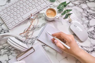 Kadın el yazısı, defter, gözlük, kulaklık ve beyaz mermer arka plan görünümlü aksesuarlarla işyeri modeli. Kadınsı çalışma tarzı konsepti.