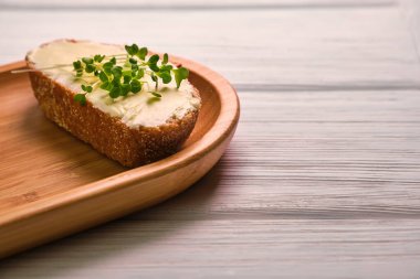 Tahta bir tabakta tereyağlı ve mikroyeşillikli ekmek dilimi, açık ahşap bir arka planda.