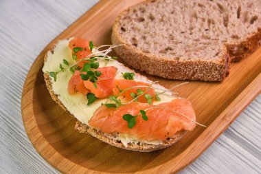 Füme somon ve ahşap arka planda tereyağlı bir dilim ekmek. Mayasız ekmek yağı, mikroyeşil ve tahta tabakta balık. Lezzetli aperatif ya da aperatif. Kapat.