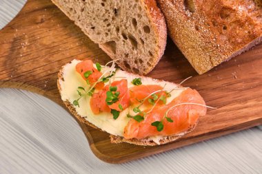 Füme somon ve ahşap arka planda tereyağlı bir dilim ekmek. Mayasız ekmek yağı, mikroyeşil ve tahta kesme tahtasındaki balıklar. Lezzetli aperatif ya da aperatif. Kapat.