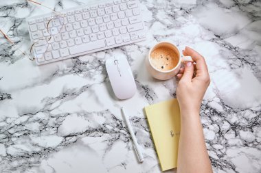 Düz uzanın, ofis masasında Girl 'ün elinde kahve var. Klavye, malzeme, mermer arka planda bir fincan kahve. Kahve molası, fikirler, notlar, hedefler veya plan yazma konsepti. Üst görünüm