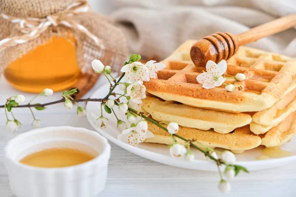 Taze Belçika waffle 'larının üzerine bal dökülüyor. Mineral ve vitamin açısından zengin organik sağlıklı bahar kahvaltısı. Kahvaltı için eko-yemek. Kiraz çiçekleriyle moda tatlı şekerlemeler