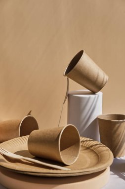 Çevre dostu sofra takımı, ahşap çatallar, tabaklar ve bardaklar modaya uygun podyumlar ve geometrik kaideler, açık bej arka planda soyut kompozisyon.