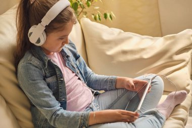 Sıradan kıyafetler ve kulaklıklar takan, tablet kullanan ve odada bir kanepede oturup müzik dinleyen tatlı bir kız..