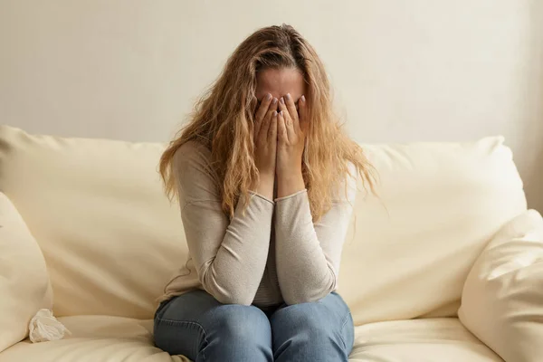 Indoor image of sad and stressed young woman covering her face with her hands and crying at home.